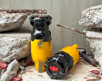 May include: Two yellow and black grenade-shaped objects with red accents. The objects are sitting on a gray concrete surface with some debris.