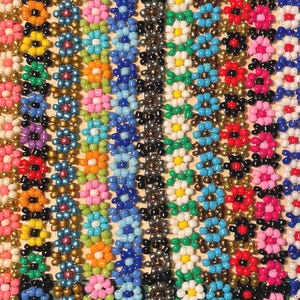 May include: A close-up of a variety of colorful beaded bracelets with flower designs. The bracelets are made with small, round beads in various colors, including pink, blue, green, yellow, and red. The flower designs are created by using different colored beads to form the petals and centers of the flowers.