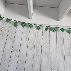 Może przedstawiać: Girlanda świetlna z zielonymi żarówkami w kształcie liści, wisząca z białego sufitu.