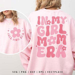 Könnte beinhalten: Ein hellrosa Sweatshirt mit dem Text "IN MY GIRL MOM ERA" in Rosatönen. Auf der Vorderseite des Sweatshirts befindet sich eine Blumengrafik mit den Worten "GIRL MOM ERA" darum. Das Design enthält Sternakzente.