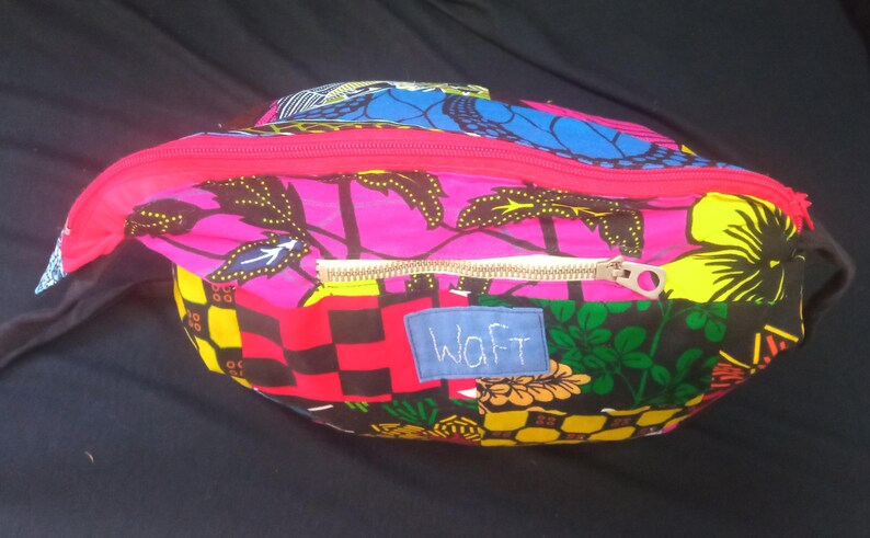 May include: A colorful zippered pouch with a pink, black, yellow, and blue patterned fabric. The pouch has a gold zipper and a white label with the word "Waft" written in black.