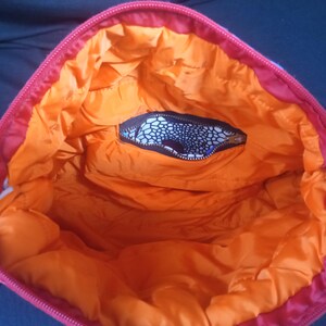 May include: The inside of a red and orange bag with a black and white patterned pocket. The bag is lined with orange fabric.