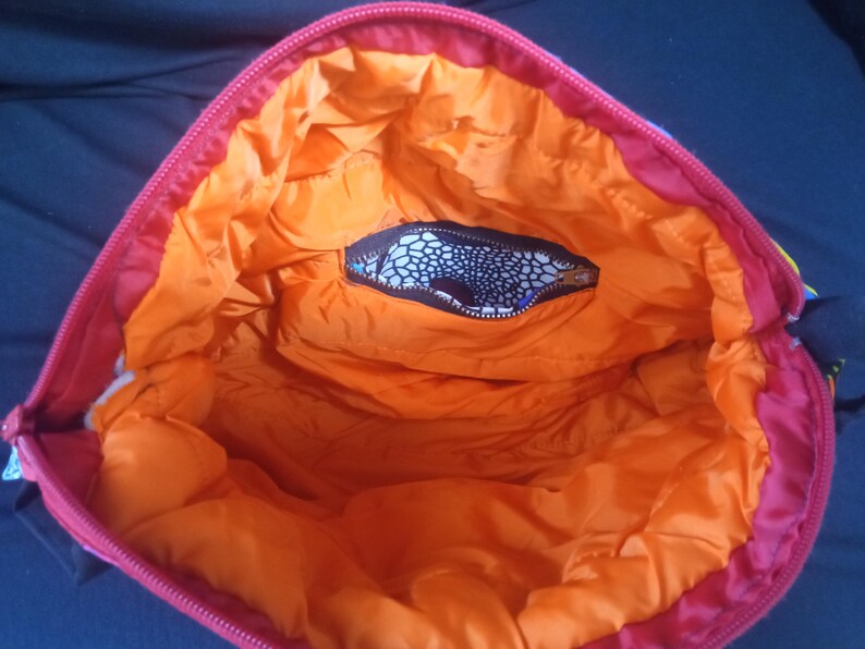 May include: The inside of a red and orange bag with a black and white patterned pocket. The bag is lined with orange fabric.