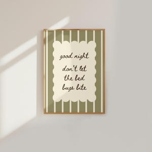 May include: A rectangular wall art print in a wooden frame featuring a sage green and white vertical striped background. Centered is a cream-colored scalloped rectangle with the dark brown text: good night don't let the bed bugs bite.