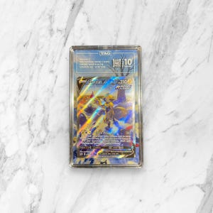 May include: A graded Pokémon card featuring Zeraora V, an alternate art ultra rare card. The card is encased in a clear plastic holder with a TAG 10 grade. The card has a colourful illustration of a Zeraora character.
