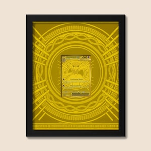 May include: Framed gold-colored artwork featuring a trading card with a character illustration and text. The card is centered within a gold-toned circular design, all set against a matching background. The black frame provides a contrasting border.