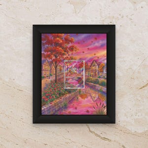 Könnte beinhalten: Gerahmtes Kunstwerk mit einer herbstlichen Landschaft mit Fluss, Brücke und Häusern. Das Gemälde hat eine warme Farbpalette aus Rot-, Orange- und Rosatönen, mit einem kleineren Bild in der Mitte. Der Rahmen ist schwarz.