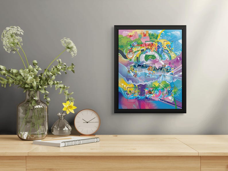May include: A framed, colorful artwork with a black border is displayed on a wooden table. The artwork features a vibrant, abstract design with various shapes and colors. A clear glass vase with green foliage and white flowers, a yellow flower in a small vase, and a clock are also on the table.