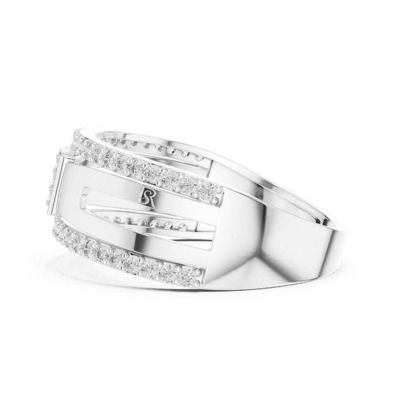 May include: A silver ring with a rectangular center stone and a band adorned with small, clear gemstones. The ring features a unique design with open spaces and a subtle 'S' marking.