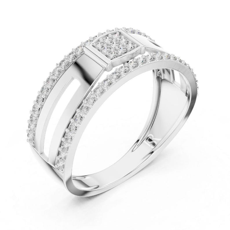 May include: A silver ring with a square center stone and a band lined with small, clear stones. The ring has a modern design with a split band and a geometric shape.