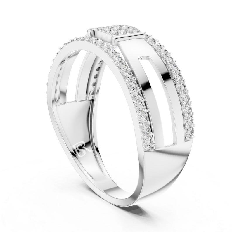 May include: A silver ring with a modern design. The ring features a rectangular top with a row of small, clear stones. The band has two parallel open sections, each lined with more small stones. The ring is set against a white background.