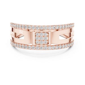 May include: Rose gold ring with a rectangular center and a band of small, sparkling diamonds. The ring has a unique design with cut-out sections and a double row of diamonds along the top and bottom edges. The ring is set against a white background.