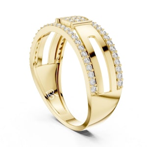May include: A gold ring with a modern design. The ring features a rectangular top with small, clear stones and two parallel bands with additional stones. The ring has a unique open design with a polished finish.