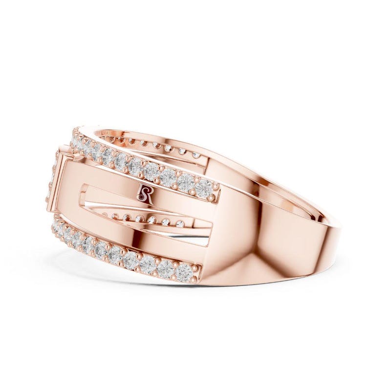 May include: Rose gold ring with a rectangular design and a row of small, clear gemstones. The ring features an open design with the letter "S" visible. The band is smooth and polished, reflecting light.
