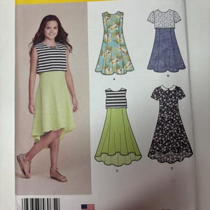 May include: Simplicity sewing pattern 8065 for sizes 8-16, featuring illustrations of four dress variations. The designs include sleeveless and short-sleeved options with various floral, striped, and solid patterns, including a high-low hemline style.