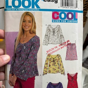 May include: A New Look sewing pattern envelope for junior sizes, featuring illustrations of various long-sleeve and sleeveless tops with tie-front details. The package displays a model wearing a blue and purple paisley print top with flared sleeves.