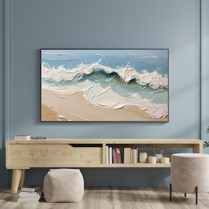 Könnte beinhalten: Abstrakte Malerei von Meereswellen in Blau-, Weiß- und Beigetönen. Das Kunstwerk wird auf einem an der Wand befestigten Fernseher über einer Holzkonsolentisch präsentiert. Das Gemälde zeigt einen strukturierten, impressionistischen Stil von brechenden Wellen.