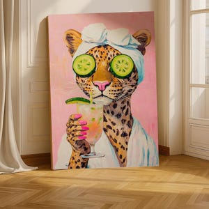 May include: A canvas print of a leopard wearing a spa headband and cucumber slices over its eyes, holding a cocktail. The leopard has a spotted coat and is set against a pink background. The nails are painted pink.