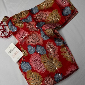 May include: A red blouse with a leaf pattern in shades of pink, blue, and gold, embellished with sequins. The blouse has long sleeves and a tag that reads "Sheetal's FabFashion Jewelry and Saree Boutique."