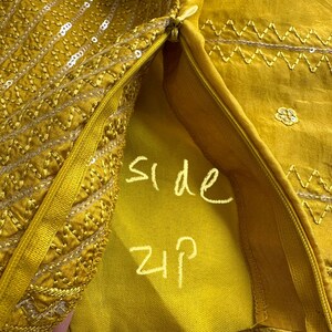 May include: Close-up of a mustard yellow garment with intricate embroidery and sequin detailing. The side zipper is visible, with the words "side zip" written in white. The fabric has a silky sheen.