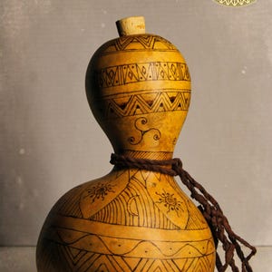 Puede incluir: Una calabaza artesanal con intrincados patrones geométricos negros y un tapón de corcho natural. La calabaza está adornada con una cuerda marrón y presenta una forma orgánica única, mostrando una mezcla de arte y funcionalidad.