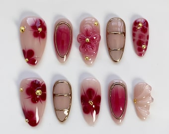 Uñas prensadas con flores color burdeos, uñas almendradas largas, uñas color burdeos, uñas con flores, uñas cromadas doradas 3D, uñas rojas y uñas festivas.