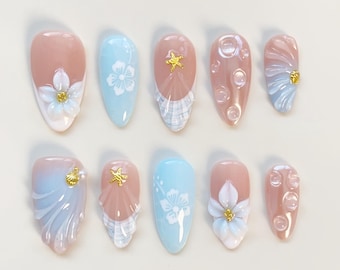 Uñas postizas en azul bebé, uñas almendradas largas, uñas con conchas 3D, uñas azules, uñas blancas, uñas kawaii, uñas festivas, uñas lindas, uñas con flores francesas.