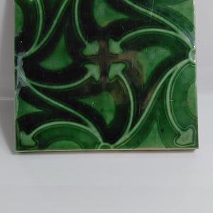 Peut inclure: Un carreau en céramique carré avec une finition brillante dans des nuances variées de vert forêt profond et d'émeraude. La surface présente un motif en relief composé de lignes entrelacées et de formes pointues en flèche symétriques.