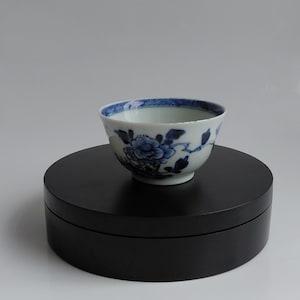 Peut inclure: Un petit bol à thé en porcelaine à base blanche orné de motifs floraux peints à la main en bleu. Le bol présente un bord évasé et un corps arrondi, décoré de fleurs et de feuilles bleues détaillées entourant l'extérieur et une bordure bleue.