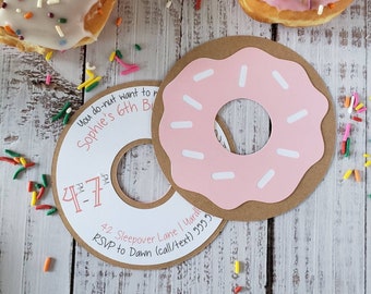 May include: Donut-shaped birthday invitations with pink frosting and white sprinkles, alongside real donuts with frosting and sprinkles. The invitations are brown with pink frosting details and include the text "You do-nut want to miss Sophie's 6th Birthday".