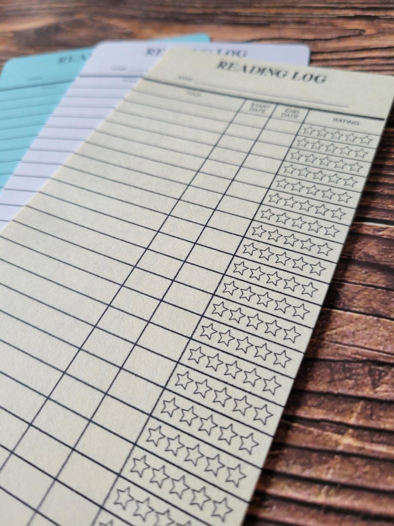 K&ouml;nnte beinhalten: Ein cremefarbenes Lesetagebuch mit einem schwarzen Raster und einer Spalte zur Bewertung von B&uuml;chern mit f&uuml;nf Sternen. Der Titel "Reading Log" ist oben auf der Seite gedruckt.