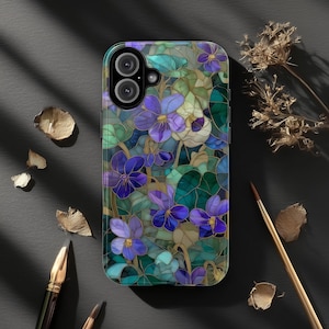 Peut inclure: Coque de smartphone ornée d'un motif de vitrail représentant des violettes violettes et des feuilles vertes. Le design présente des contours dorés et une finition brillante. L'ensemble est posé sur un fond sombre, créant un contraste saisissant.