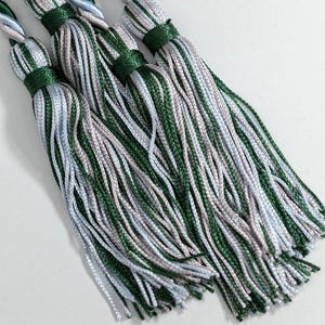 May include: Close-up of several decorative tassels. Each tassel features a green, silver, and white colour scheme. The tassels are bound with green thread and have twisted cords in matching colours.