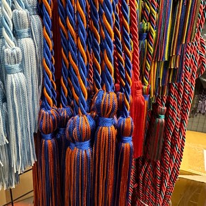 May include: A selection of decorative tassels and cords in various colours. The tassels feature blue and orange twisted cords with matching tassels. Other cords are red, blue, yellow, and green. These tassels are likely for home decor or craft projects.