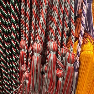 May include: A selection of decorative tassels in a variety of colours. The main focus is on red and grey tassels with twisted cords. Other tassels in the image include green, white, and red, as well as purple and yellow. These tassels are likely for home decor or craft projects.