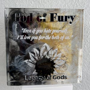 May include: Square resin art piece with the text "God of Fury" and "Legacy of Gods". The artwork features a black and white floral design with gold and black swirls. The quote "Even if you hate yourself, I'll love you for the both of us" is also included.