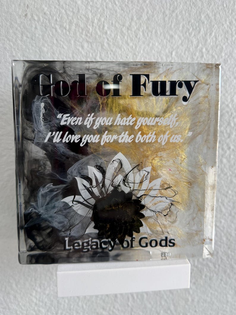 May include: Square resin art piece with the text "God of Fury" and "Legacy of Gods". The artwork features a black and white floral design with gold and black swirls. The quote "Even if you hate yourself, I'll love you for the both of us" is also included.