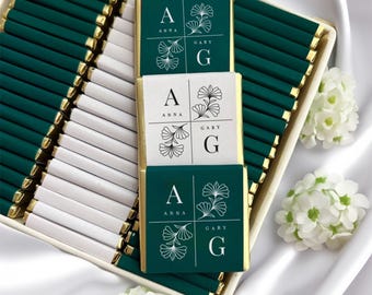 May include: A box of green and white chocolate bars with gold trim. The bars are wrapped in paper with the names "Anna" and "Gary" and the letters "A" and "G" printed on them. The bars are arranged in rows in the box.
