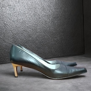 Puede incluir: Un par de zapatos de salón de cuero gris oscuro con punta afilada y tacón dorado de 5 cm. Los zapatos tienen un diseño clásico y son adecuados para ocasiones formales.