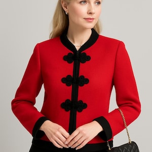 Peut inclure: Veste rouge avec garniture noire et fermetures décoratives en forme de grenouille. La veste présente un col mandarin et des manches longues. Un sac à main noir matelassé avec une bandoulière en chaîne dorée est également visible.