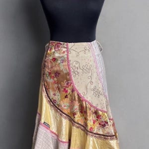 Puede incluir: Una falda colorida y en capas con un diseño floral y estampado. La falda presenta una mezcla de texturas, incluyendo satén y encaje, con una paleta de colores predominantemente amarilla y rosa. La falda se exhibe en un maniquí.