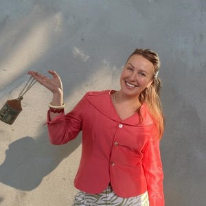 Op de afbeelding: Koraalroze blazer met een reverskraag en drie knopen, gecombineerd met een broek met zebraprint. Een kleine, huisvormige hanger hangt aan een ketting.