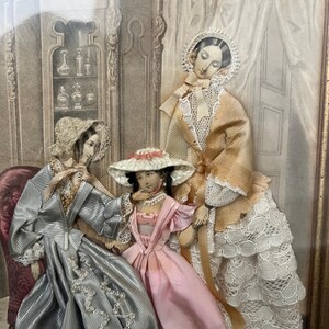 Puede incluir: Obra de arte enmarcada que presenta tres figuras con vestimenta de época. Las figuras visten vestidos largos con gorros y sombreros. La paleta de colores incluye tonos de rosa, gris y crema. La obra está ambientada en una habitación con detalles arquitectónicos.