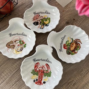 Puede incluir: Cuatro platos blancos en forma de concha con ilustraciones de mariscos. Cada plato presenta un diseño de marisco diferente, incluyendo una langosta, un cangrejo y otros crustáceos, con la palabra "Beervruchten" en escritura negra.