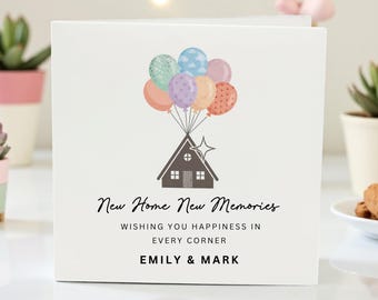 Puede incluir: Una tarjeta de felicitación blanca con una ilustración de casa y globos. La tarjeta dice "New Home New Memories" con los nombres "Emily & Mark" en la parte inferior. Los globos son de varios colores, incluyendo azul, rosa y naranja.