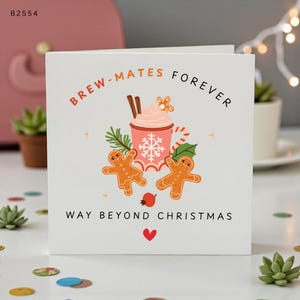 Puede incluir: Una tarjeta de felicitación cuadrada blanca con una ilustración central de una taza rosa con diseño de copo de nieve, cubierta con nata montada y ramas de canela. Dos galletas de jengibre, ramas de pino y una baya roja rodean la taza. El texto dice: BREW-MATES FOREVER WAY BEYOND CHRISTMAS con un pequeño corazón rojo.