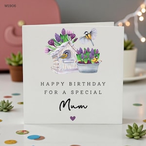 Op de afbeelding: Een vierkante witte wenskaart met een aquarelillustratie van een houten vogelhuisje, een metalen emmer gevuld met paarse bloemen en drie kleine vogels. De tekst luidt HAPPY BIRTHDAY FOR A SPECIAL Mum met een klein paars hartje eronder.
