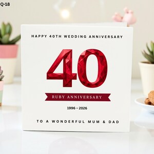 May include: A white card with the text "HAPPY 40TH WEDDING ANNIVERSARY" and "RUBY ANNIVERSARY." A large, faceted red number "40" is centered on the card. The text "1996-2026" and "TO A WONDERFUL MUM & DAD" are also present.