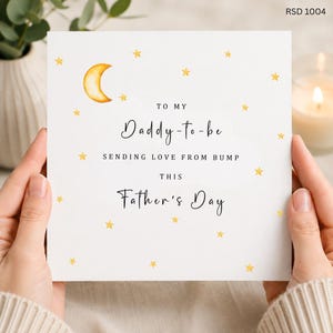 May include: A white Father's Day card with gold stars and a crescent moon illustration. The card reads "To My Daddy-to-be, Sending Love From Bump, This Father's Day."