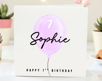 Op de afbeelding: Een witte verjaardagskaart met een lichtpaarse ballon met het nummer 7 en de naam "Sophie" in zwart schrift. De tekst "HAPPY 7TH BIRTHDAY" staat onderaan.